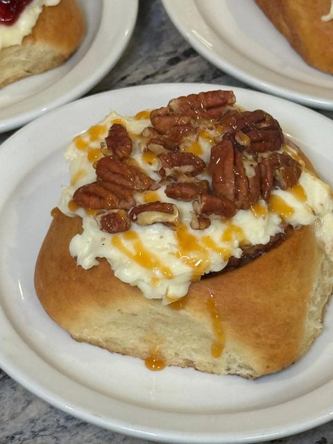 Cinnamon roll topped with cream-cheese frosting, pecans and caramel