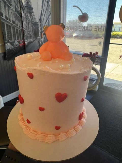 Pink cake covered in red hearts with a teddy bear on top