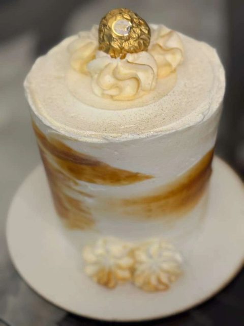 White naked cake brushed with gold and topped with a gold sugar ball